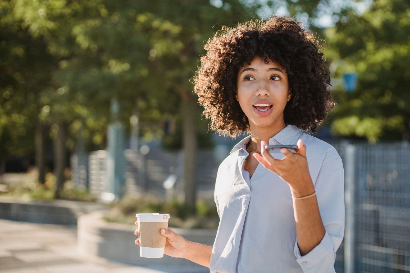 Woman speaking a command into her phone while out with a coffee